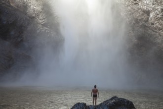Daytime scene at Wallaman Falls with a fit man in swim trunks below the waterfall, Queensland,
