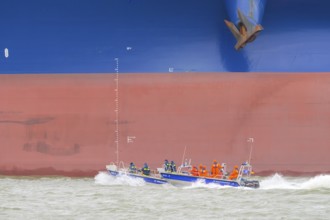 THW lifeboat with crew in orange clothing sails in front of a large ship hull on rough water,