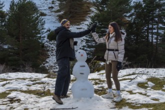 Young couple enjoying winter vacation, high fiving, and smiling while building a snowman on a snowy