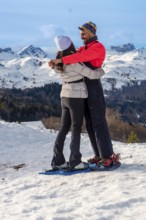 Happy couple embracing each other while snowshoeing on a snowy mountain landscape, enjoying a