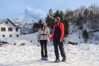 Happy couple holding hands while snowshoeing on a sunny winter day, enjoying active leisure time in
