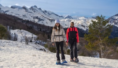 Couple snowshoeing on a snowy mountain trail, smiling and looking at the camera, with majestic snow