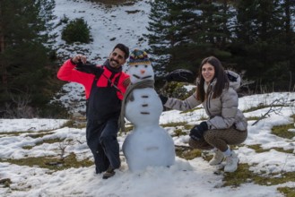 Couple building a snowman together on a snowy mountain slope, smiling and bundled in winter gear,