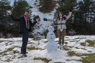 Smiling couple posing with a freshly built snowman during winter vacation, celebrating connection,