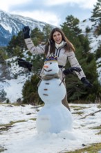 Young woman smiling and waving beside a snowman in a sunny mountain forest, enjoying winter