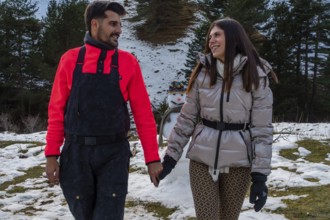 Smiling young couple enjoying a winter walk in the snowy mountains, hand in hand, with a snowman