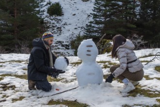 Young couple building a snowman on a sunny mountain slope, laughing and bonding in warm winter