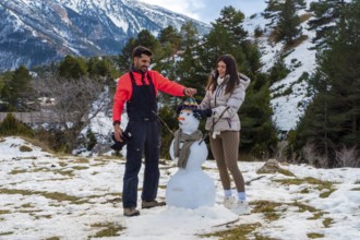 Young couple joyfully building a snowman together in a snowy mountain landscape, celebrating winter