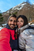 Smiling young man and woman capturing a selfie together during a snowy winter vacation, enjoying