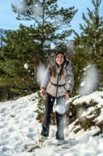 Young woman smiling and catching falling snow in a sunlit pine forest on a mountain winter