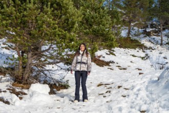 Young woman wearing warm winter clothes and a shiny jacket smiling while standing on a snowy