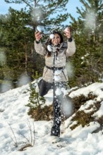 Young woman in casual winter clothes laughing and throwing snowballs in a sunlit snowy forest,