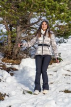 Young woman smiling and spreading her arms, dressed in warm winter clothing with a metallic jacket