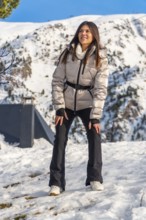 Woman standing in snow looking away, wearing winter coat and black pants, enjoying the fresh air