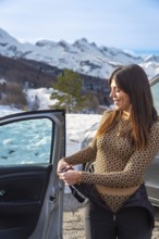Young woman by her car smiling as she adjusts ski pants, readying gear for a sunny day of winter