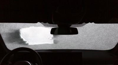 View from a car through a peephole and a windshield partly covered with snow in winter