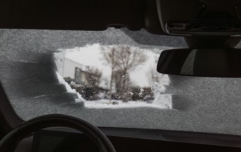 View through a peephole of a partially cleared icy car window with snow showing winter