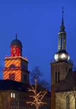 The Christmassy illuminated town hall tower and the illuminated church tower of St. John's Church
