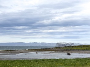 Coast with green shore, wooden racks for drying stockfish and cloudy sky over the sea, Nesseby,
