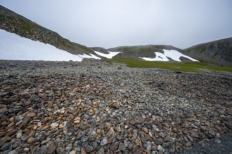 Barren mountain landscape with stones, snow and foggy sky, looks cold and rough, beach walls on