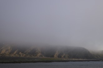 Misty coastal landscape with rocks creating a mystical and gloomy atmosphere, Båtsfjord, Finnmark,