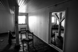 An empty interior of a house, black and white, with old wooden floors and a few chairs, Vardø,
