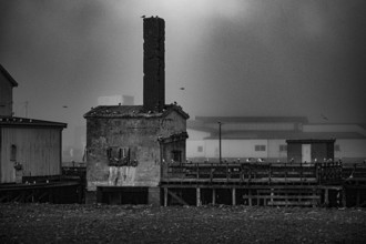 Abandoned industrial building in the old port of Vardö with a chimney in a foggy environment,