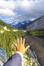 Tourist extending a hand towards the breathtaking valley view from the glass platform of the