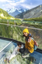 Mother and child waving from the glass platform of the glacier skywalk, enjoying the stunning