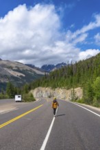 Hiker walking on the icefields parkway in the canadian rockies with a camper van parked on the side