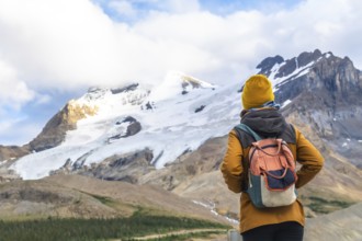 Female tourist wearing a yellow woolen hat and carrying a backpack is contemplating athabasca