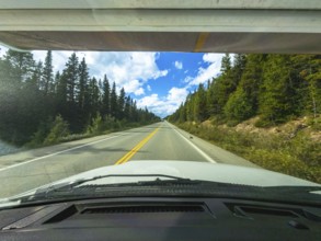 White car driving on a scenic highway through a coniferous forest in the canadian rockies on a
