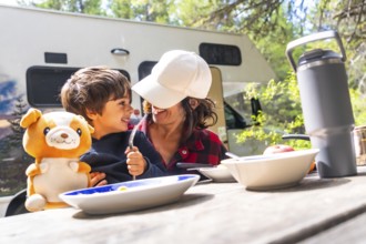 Mother and son are sitting at a picnic table, enjoying breakfast outside their campervan in banff