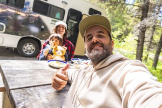 Happy family taking a selfie while having lunch on a wooden table near their camper van in the
