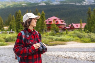 Female tourist holding binoculars enjoying the landscape of bow lake with the red roof of num ti