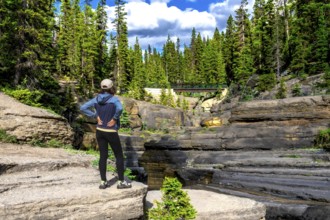 Female hiker standing on a rock formation admiring the layered rock formations of mistaya canyon