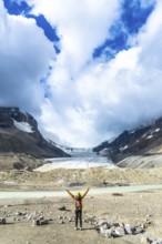 Female hiker with backpack and yellow jacket raising arms in front of the athabasca glacier, in the