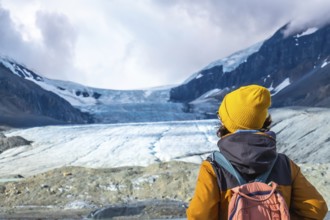 Female hiker in a yellow beanie and backpack enjoying breathtaking views of athabasca glacier in