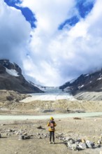 Female tourist wearing yellow jacket and backpack admiring the stunning view of the athabasca