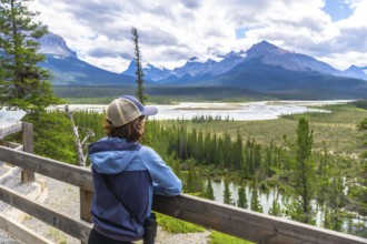 Tourist wearing a baseball cap leans on a wooden fence, admiring the stunning panorama of the north