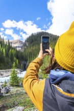 Female hiker capturing scenic waterfall photos with a smartphone along ci fuentes path on the