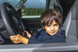 Young child playing driver while holding the steering wheel inside a car, enjoying a road trip on