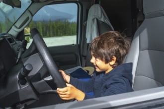 Happy child pretending to drive a vehicle while enjoying a scenic road trip through the mountains