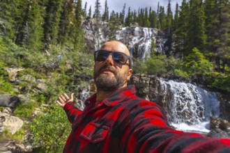 Tourist wearing sunglasses and red and black shirt taking selfie with outstretched arm in front of