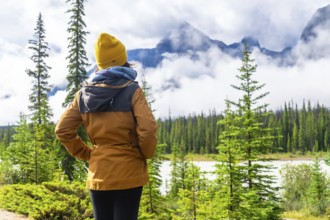 Tourist enjoying breathtaking view of majestic, cloud shrouded mountains and serene lake along