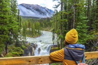 Young hiker wearing a yellow beanie and jacket admiring the stunning view of sunwapta falls in