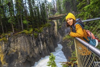 Female tourist in a yellow jacket and beanie leaning on a metal railing, admiring the stunning view