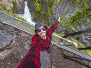 Photographer wearing sunglasses and a bucket hat takes a selfie at sunwapta falls in jasper