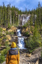 Hiker in a yellow jacket and beanie contemplating the cascading waters of tangle creek falls in