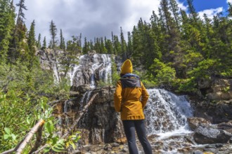Female hiker wearing yellow jacket and beanie contemplating tangle creek falls in jasper national